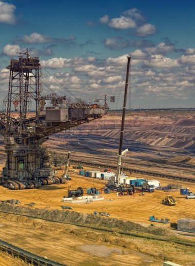 Aerial view of heavy machinery operating in a vast open-pit mine under a cloudy sky.